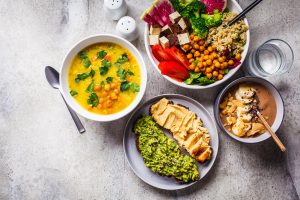 A table of plant-based dishes: lentil soup, a tofu and chickpea bowl, avocado and hummus toast, and a smoothie bowl