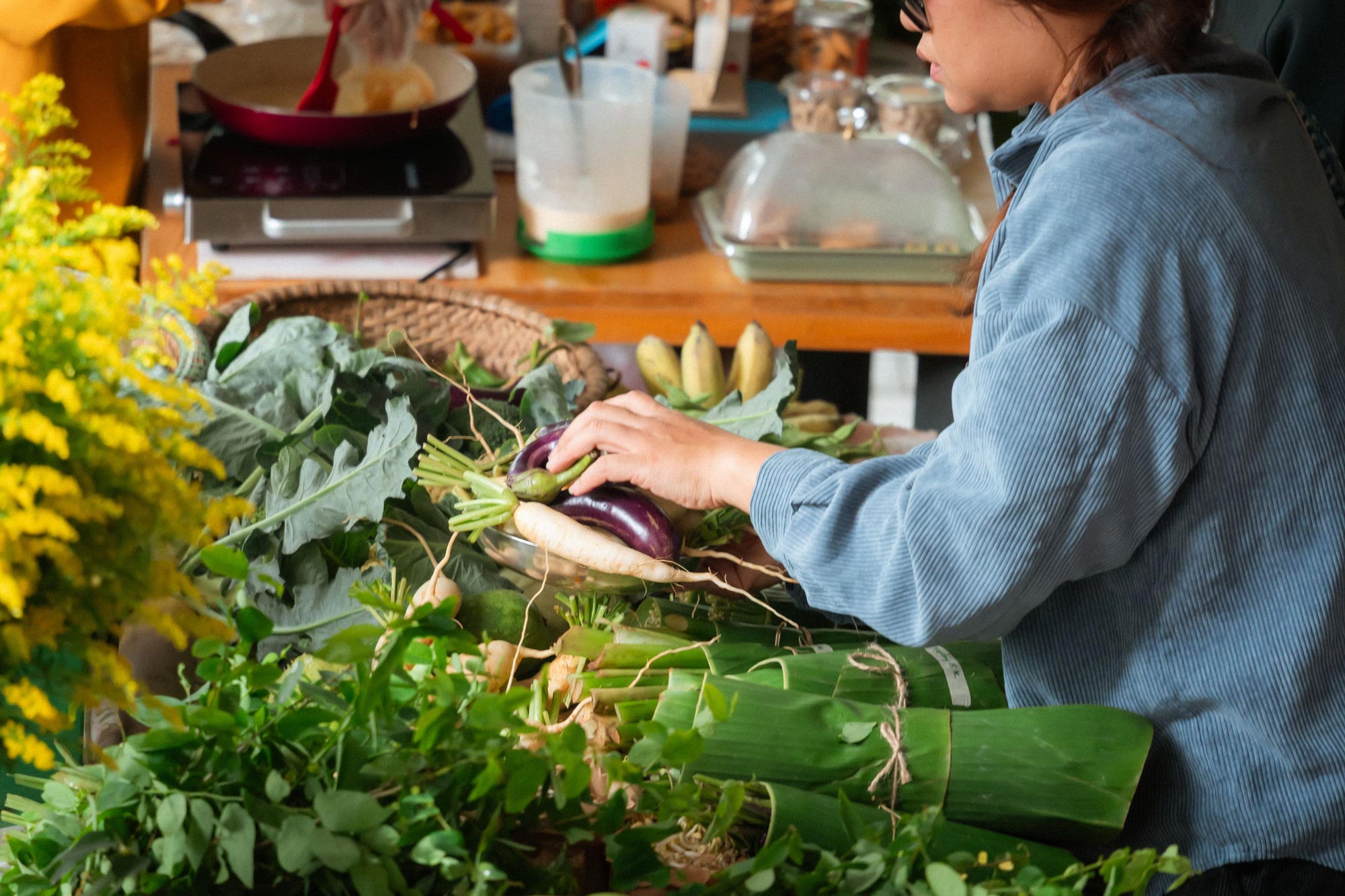 A shopper picks through fresh vegetables and leafy greens at a market stall