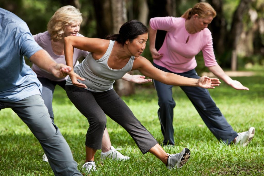 A group of adults practise tai chi together on a park lawn