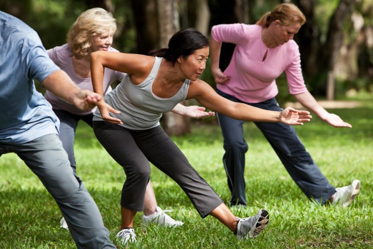 A group of adults practise tai chi together on a park lawn