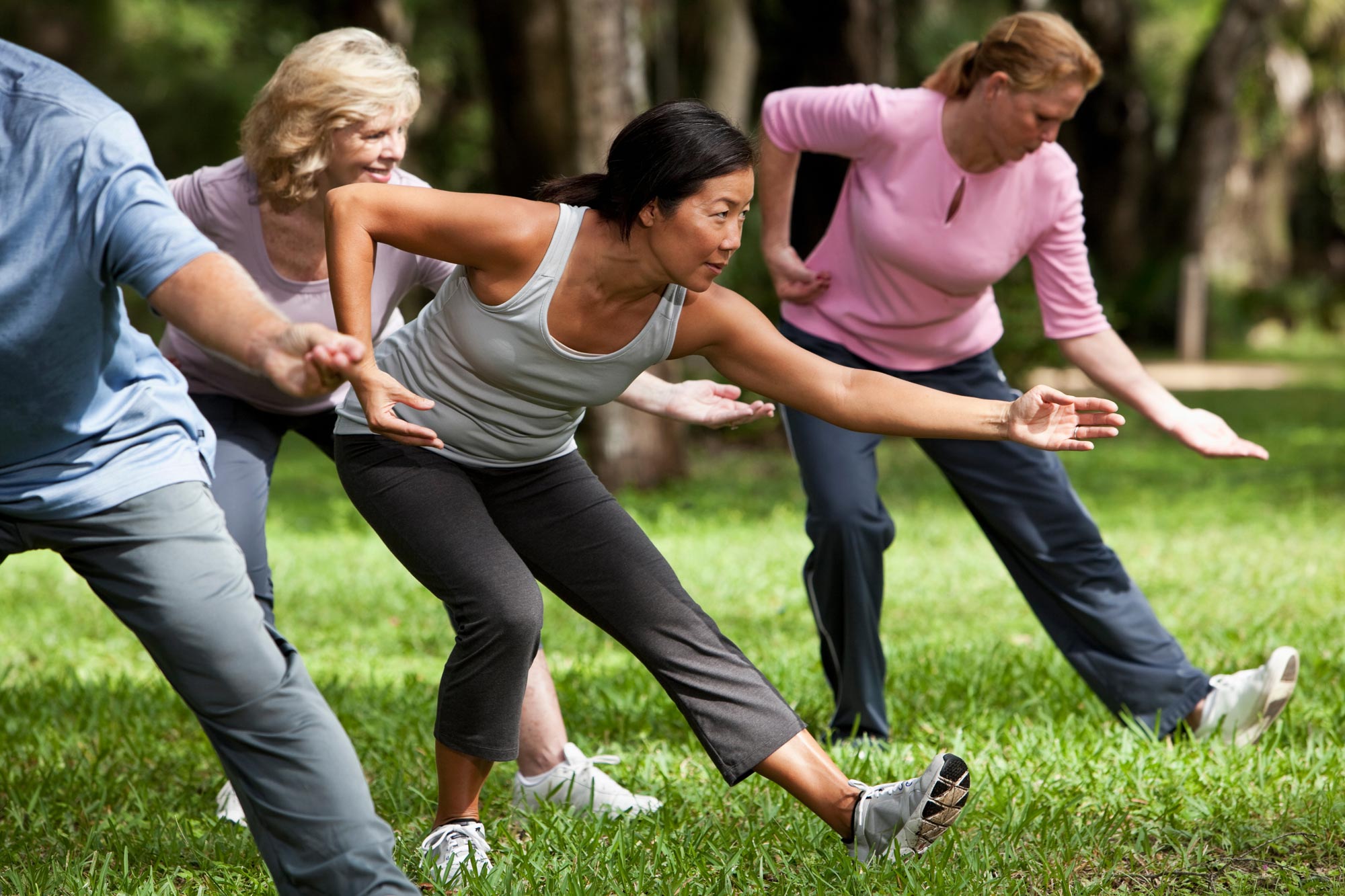 A group of adults practise tai chi together on a park lawn