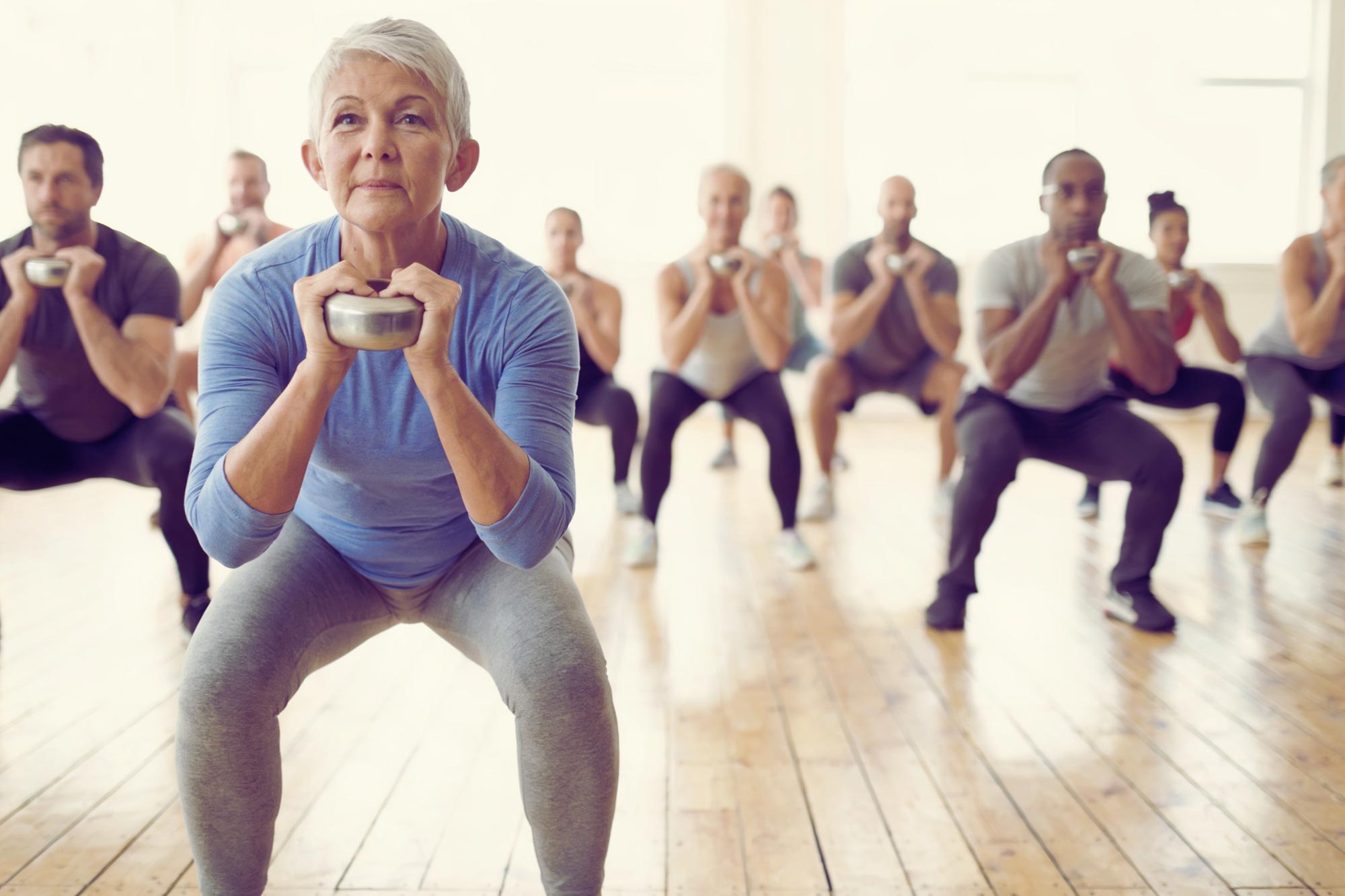 A woman in her fifties holds a kettlebell in a squat during a group strength class